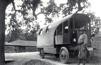 black and white photo of a man in a hat posing next to a van-like structure