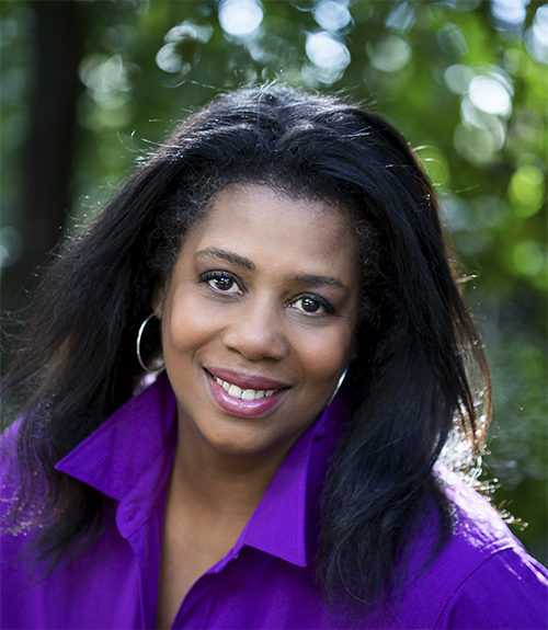 a Black woman with silver hoops and a purple shirt smiles for a head shot