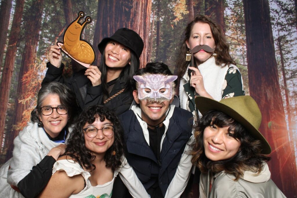 A group of people pose for a photo in a photobooth, some wearing animal masks