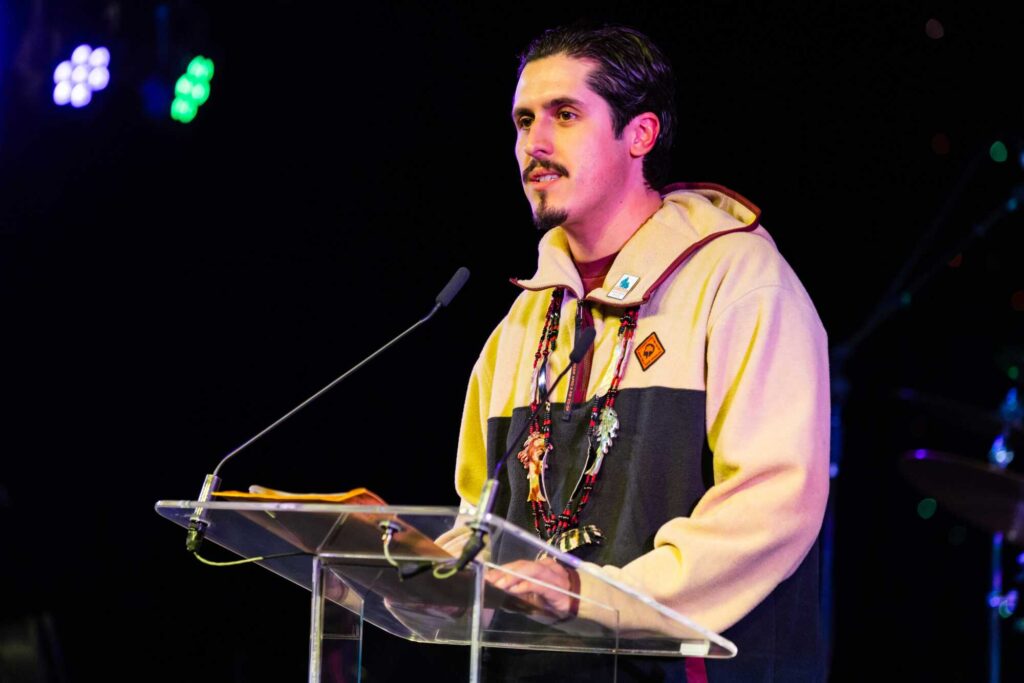 A young man stands at a podium against a very dark black background