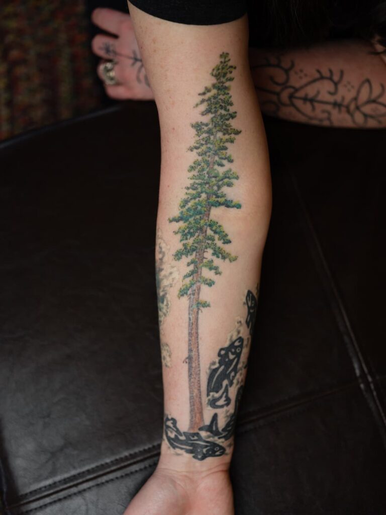 A redwood tattoo that spans across the forearm and elbow, colored green and brown.