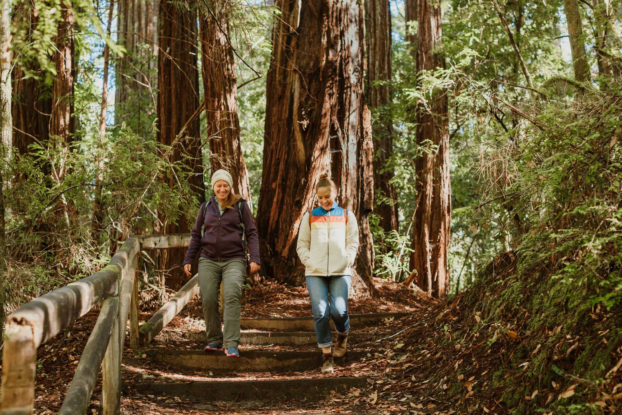 Two women in light puffy jackets walking down a redwoods trail