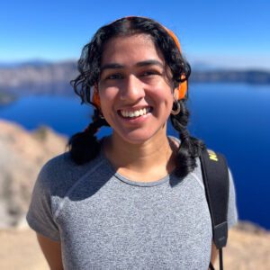 A woman with two braids poses in front of a body of water
