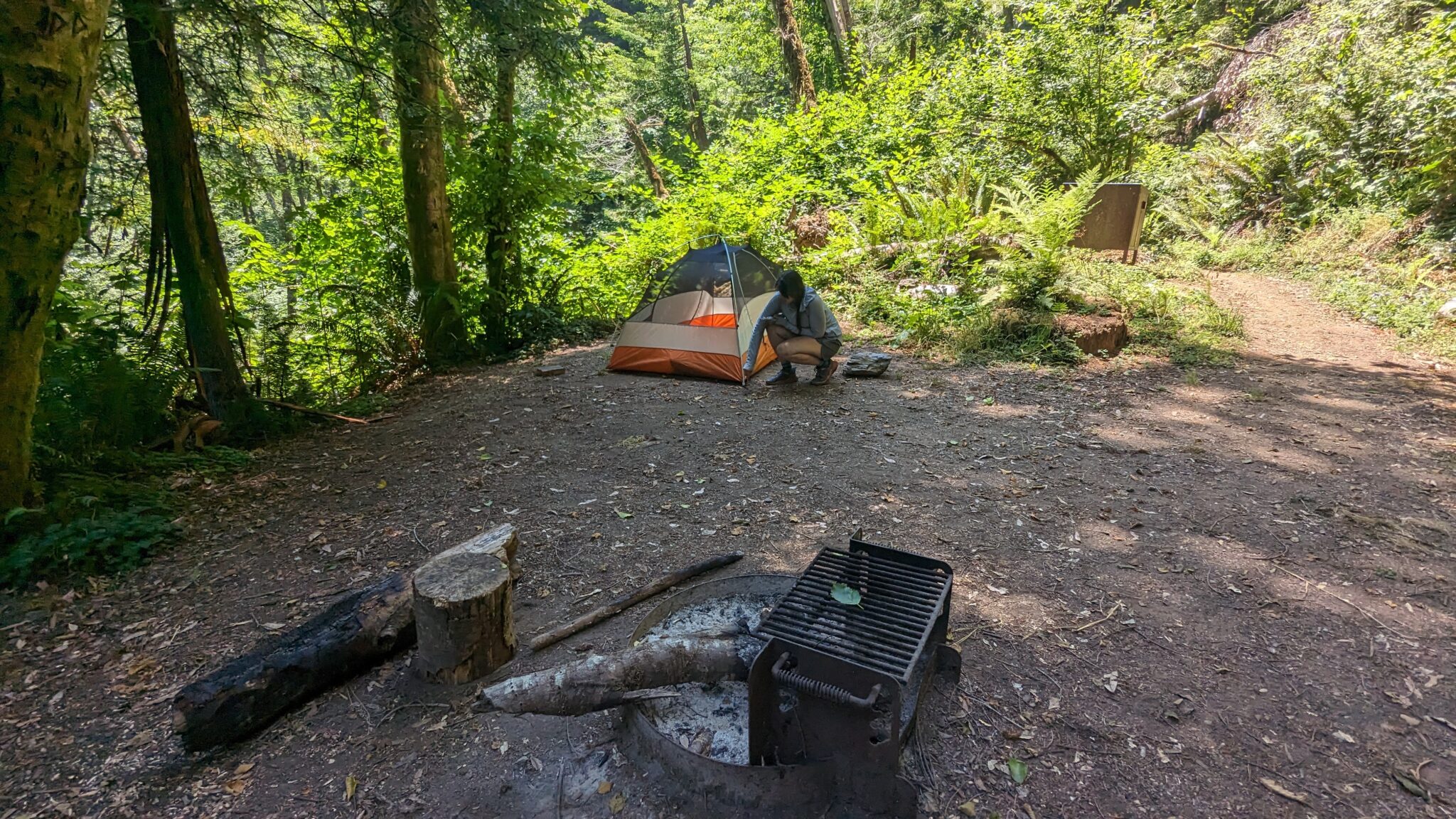 A woman sets up a small orange tent at a campground