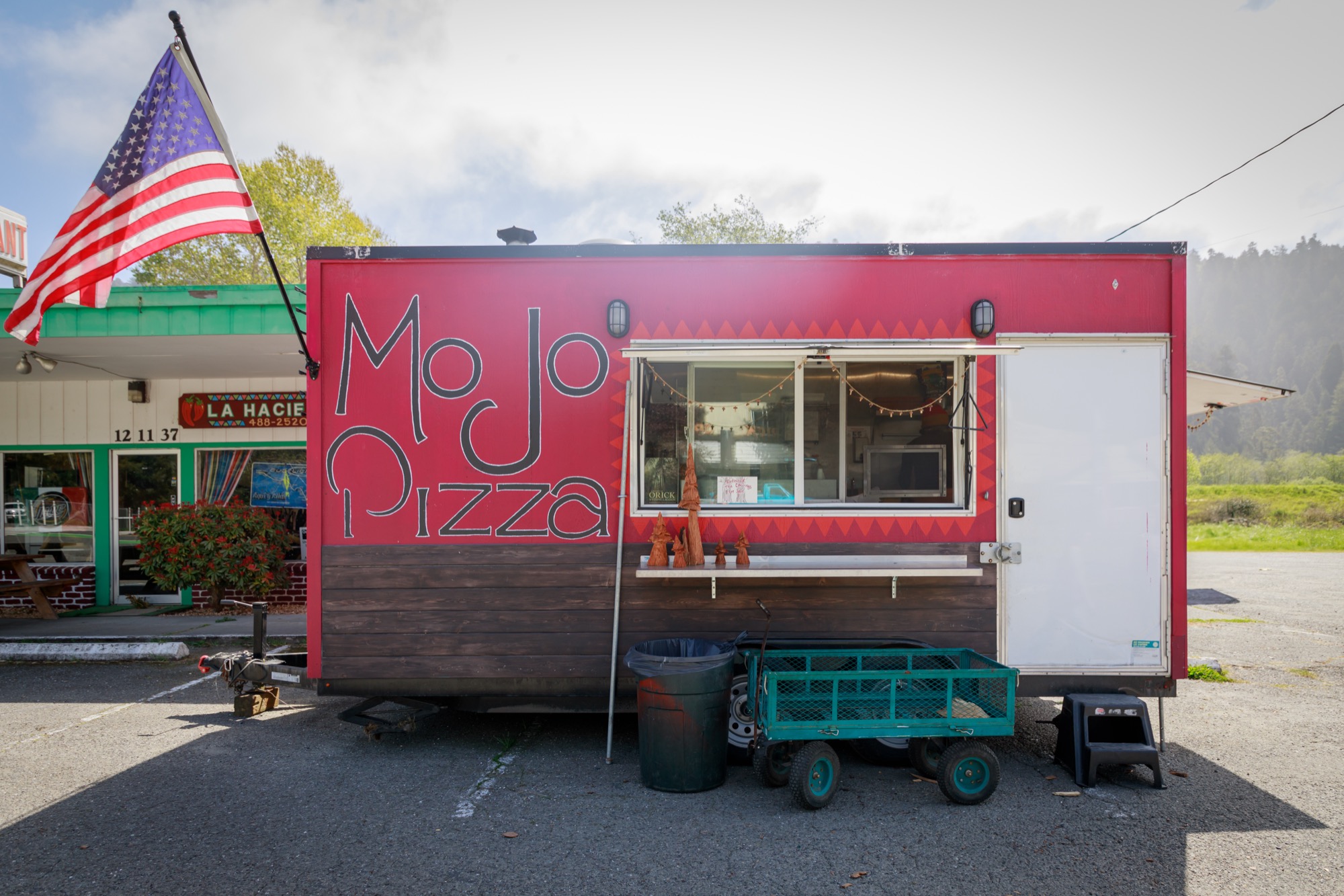 A little red trailer with a sign that reads Mojo Pizza and an American flag
