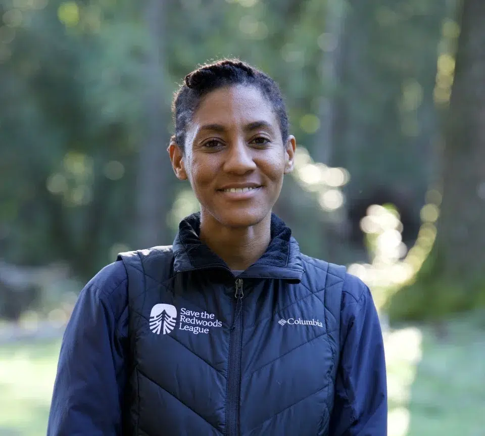 a professional headshot of a woman with short hair against a green forested background