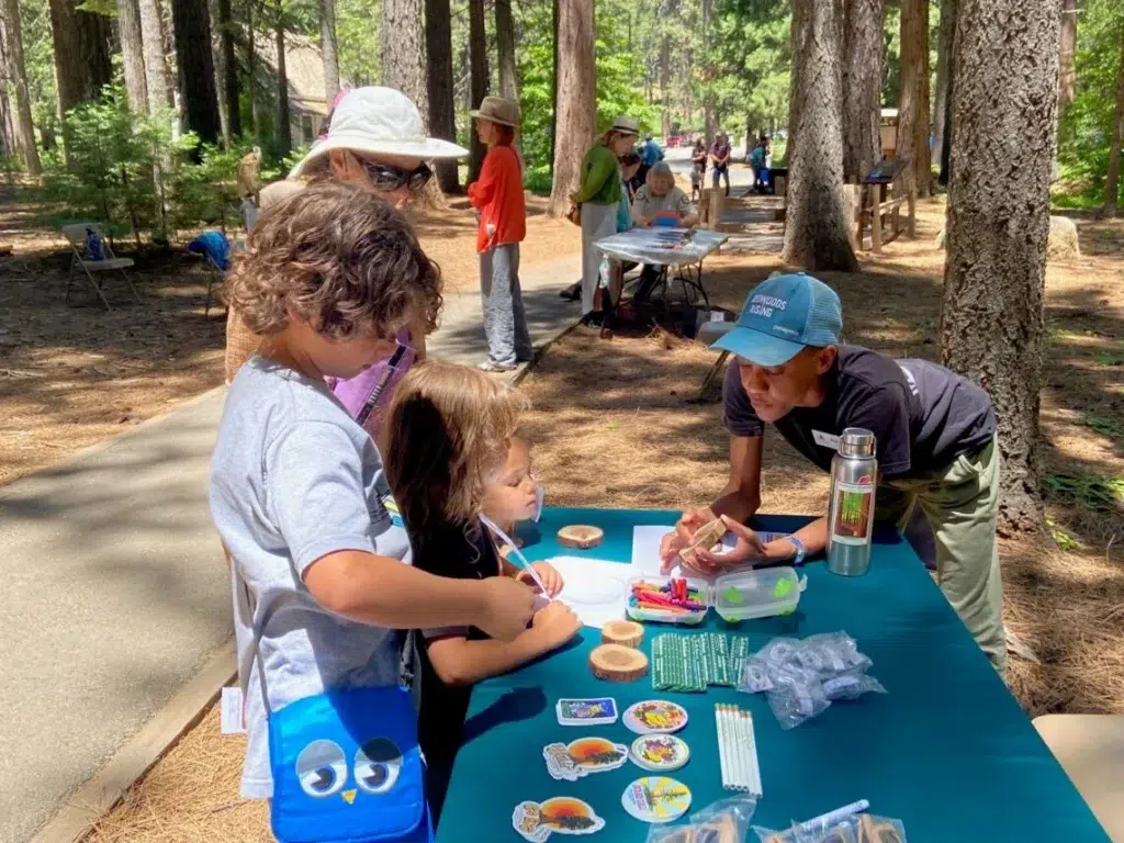 children at a table with stickers and interactive activities as a woman leans over the table to engage with them